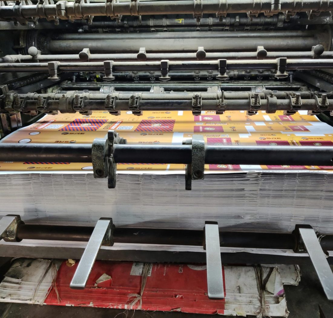 pexels-photo-9550363-9550363 Close-up of an industrial printing machine processing paper sheets in a factory setting.